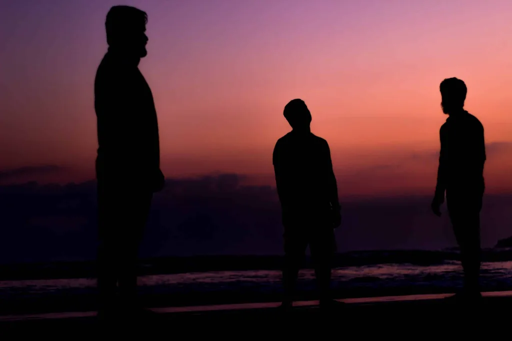 Tre uomini in piedi al tramonto, visibili solo come sagome.